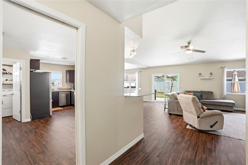 A view from a hallway into a kitchen and a living room with wood flooring — 8405 SOMERSET DRIVE, LARGO, FL