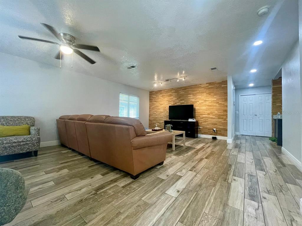A living room features a wood-paneled accent wall, a brown leather sofa, and wood-look flooring — 1044 NIN STREET, ORLANDO, FL