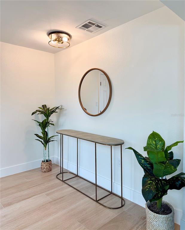 An entryway features a console table, a round mirror, two potted plants, and light wood flooring — 156 N BLVD OF THE PRESIDENTS, SARASOTA, FL