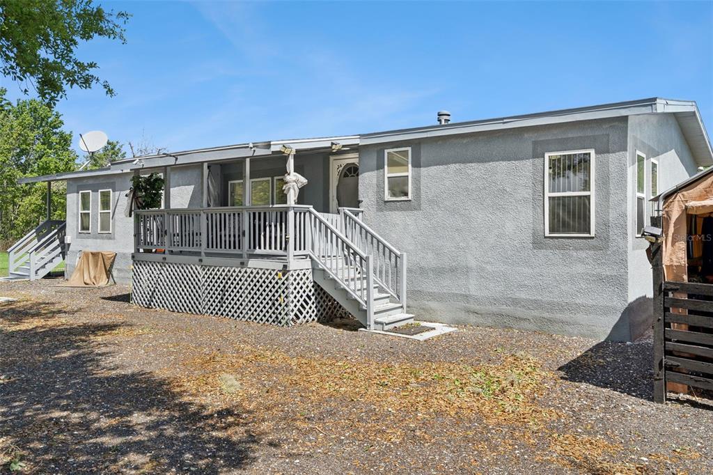 A gray single-story house features a wooden deck with stairs and a gravel yard — 2051 TRAIL CUT ROAD, POLK CITY, FL