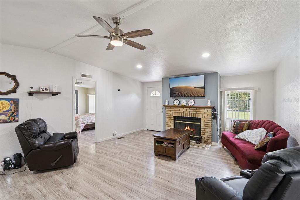 A living room features light wood-look flooring, a brick fireplace, and a ceiling fan — 2051 TRAIL CUT ROAD, POLK CITY, FL