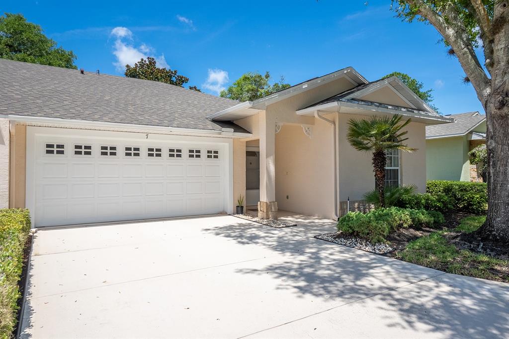 A beige single-story house features a two-car garage, a covered entryway, and a palm tree — 7 ARBOR TRACE UNIT 2, PALM COAST, FL