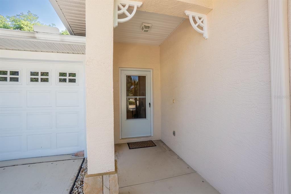 A covered entryway features a white front door, a garage door, and decorative corner brackets — 7 ARBOR TRACE UNIT 2, PALM COAST, FL