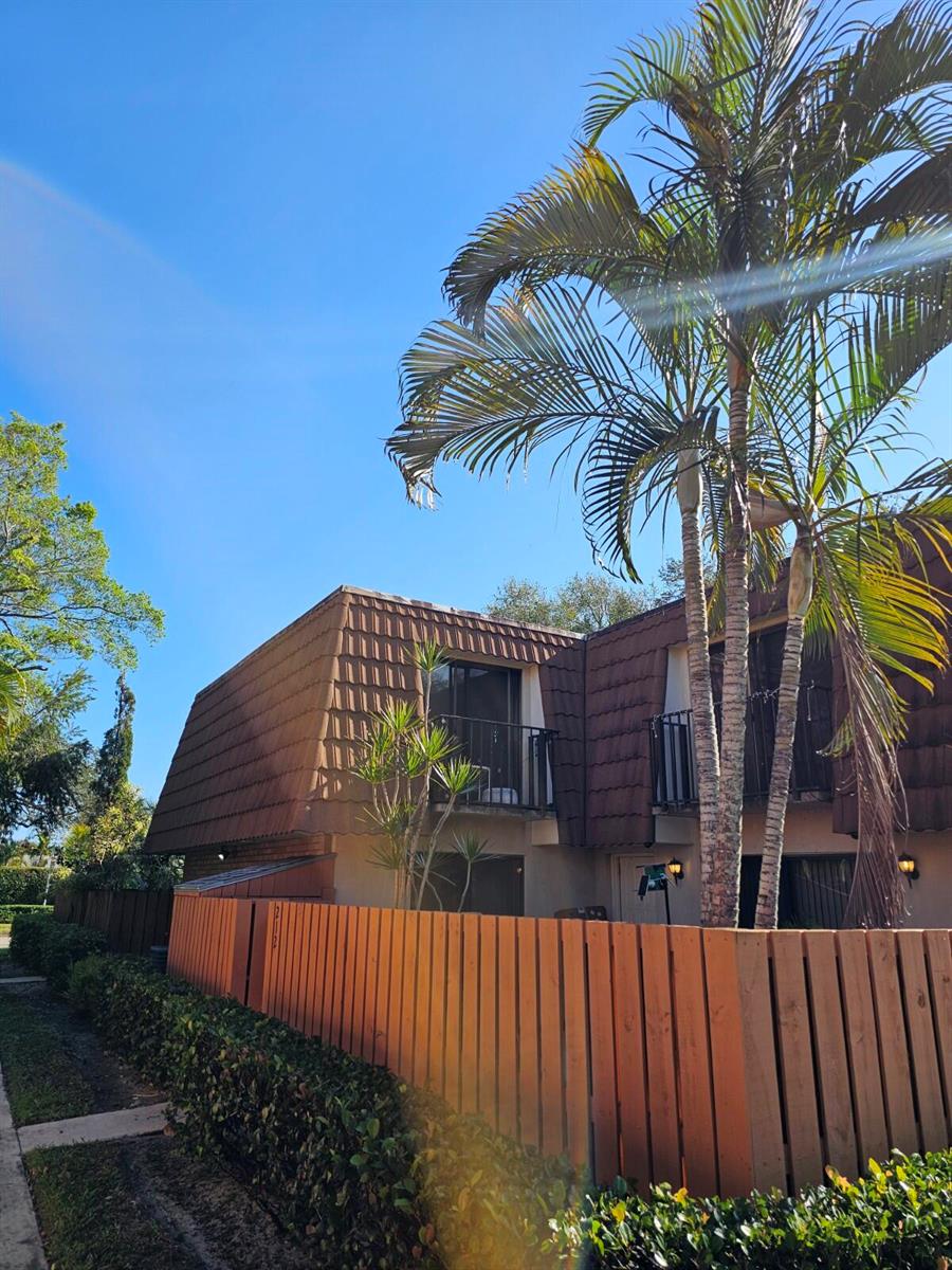 A two-story townhouse exterior with a brown mansard roof, wooden fence, and tall palm trees — 209 Charter Way, West Palm Beach FL 33407, WEST PALM BEACH, FL