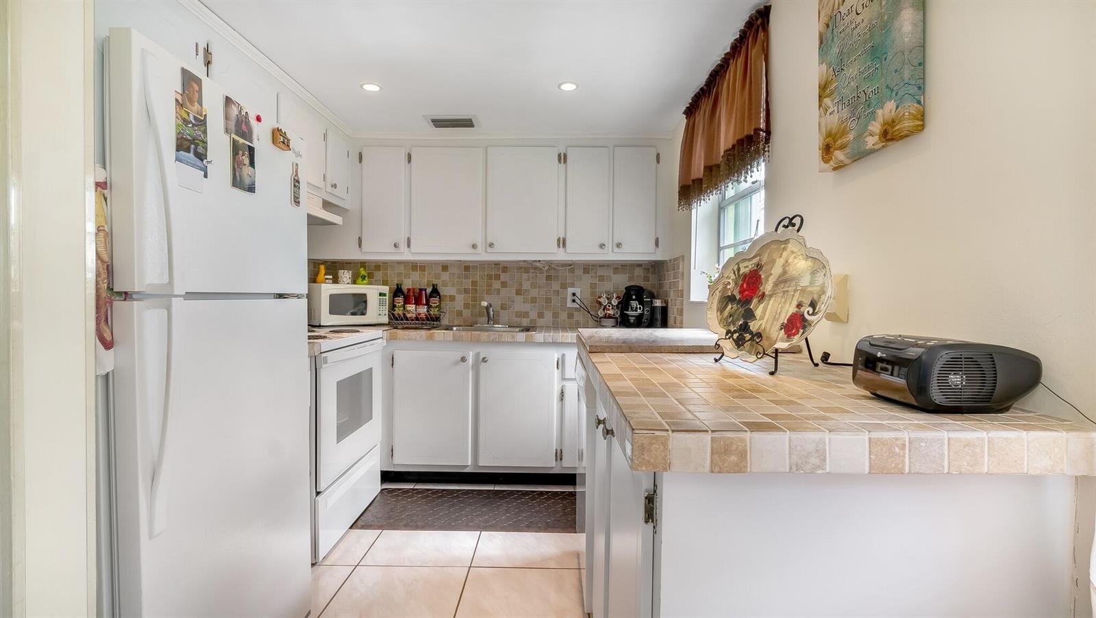 A kitchen features white cabinets, tiled countertops, a white refrigerator, and a tiled backsplash — 239 Windsor K, West Palm Beach FL 33417, WEST PALM BEACH, FL