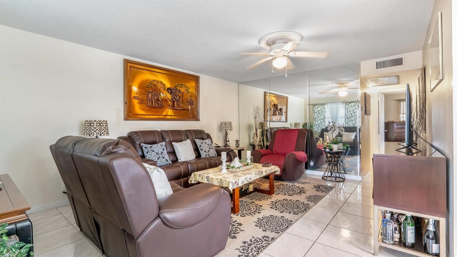 A living room features a brown leather sofa, a red armchair, and mirrored wall panels — 239 Windsor K, West Palm Beach FL 33417, WEST PALM BEACH, FL