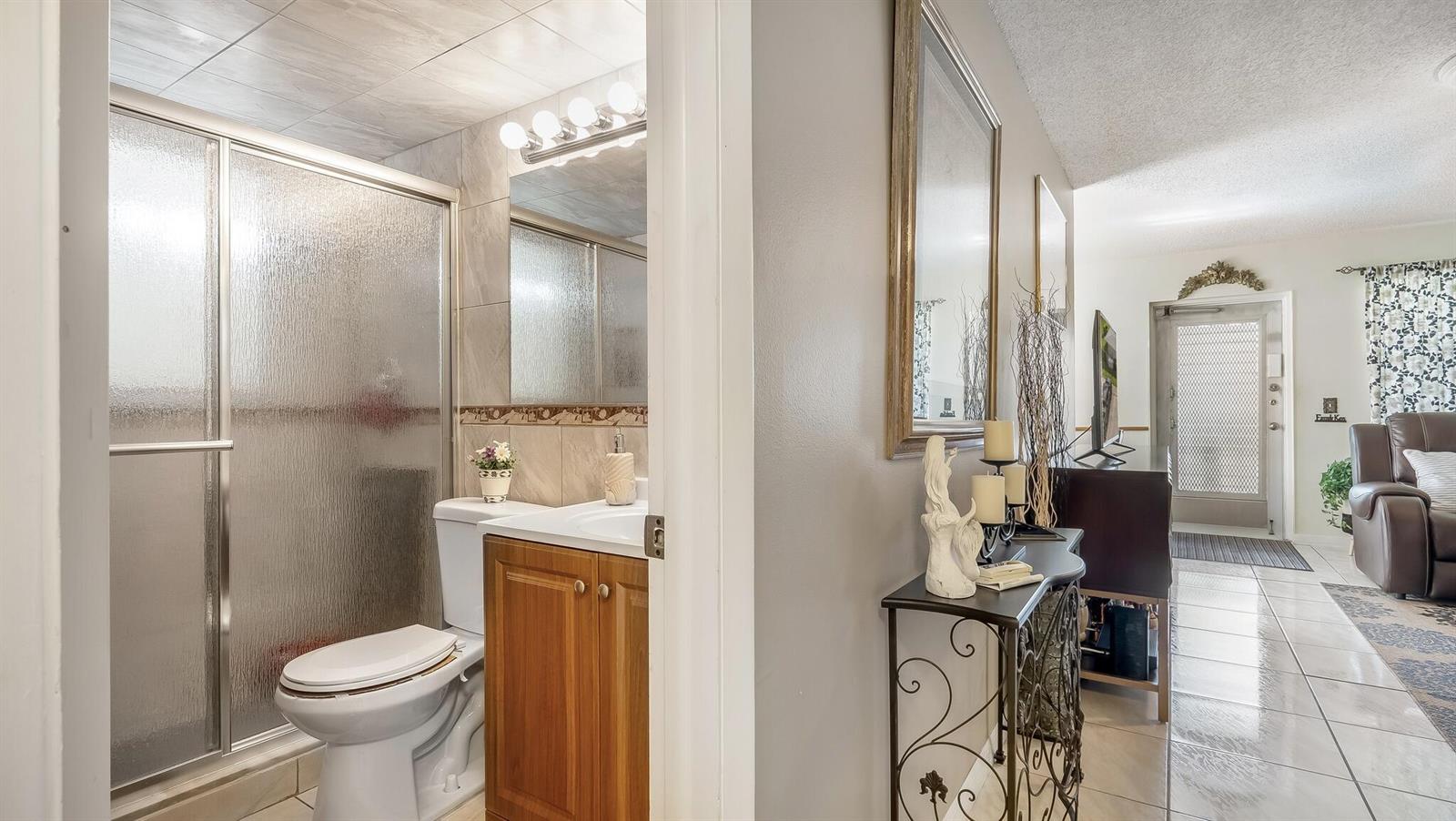 A bathroom with a shower stall and vanity sits beside a hallway with a console table — 239 Windsor K, West Palm Beach FL 33417, WEST PALM BEACH, FL