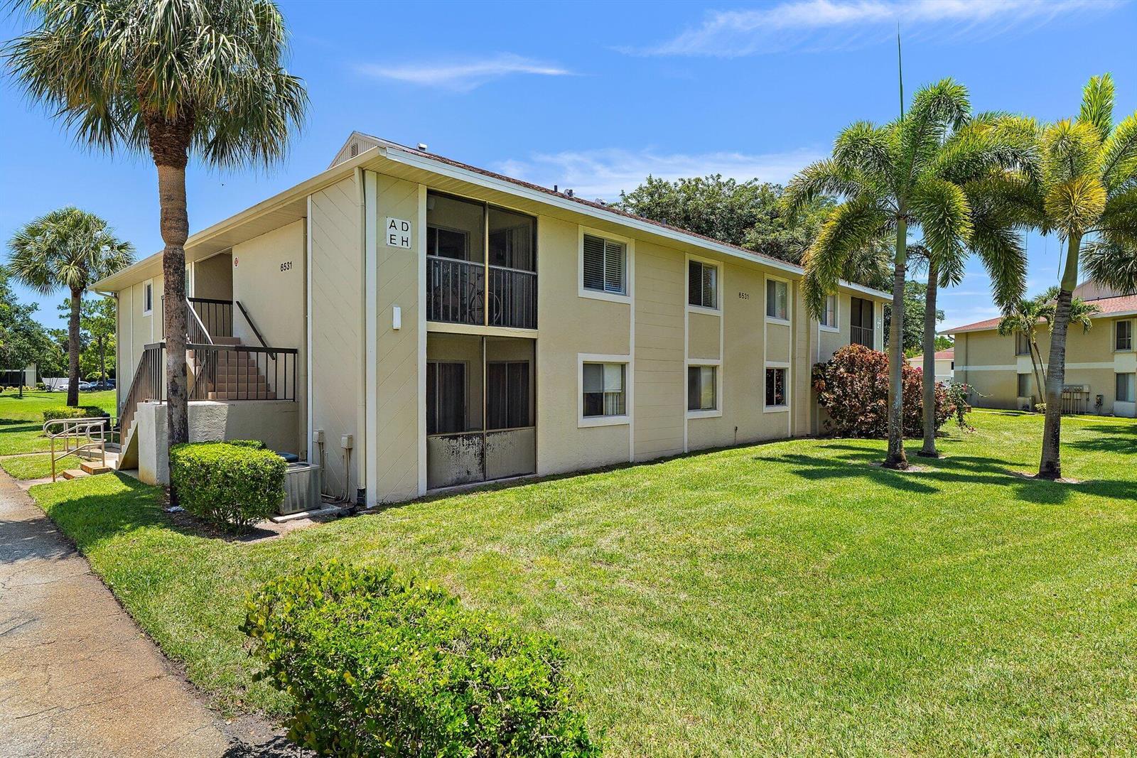 A two-story apartment building with beige siding, screened balconies, and palm trees on a lawn — 6531 Chasewood Drive # H, Jupiter FL 33458, JUPITER, FL