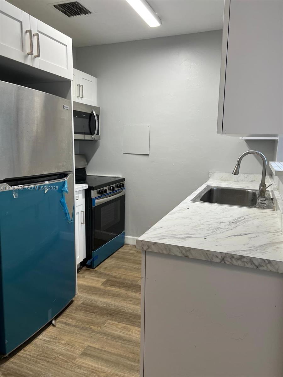 A galley kitchen features white cabinets, stainless steel appliances, and a marble-patterned countertop — 130 NE 171st Ter, Miami FL 33162, MIAMI, FL