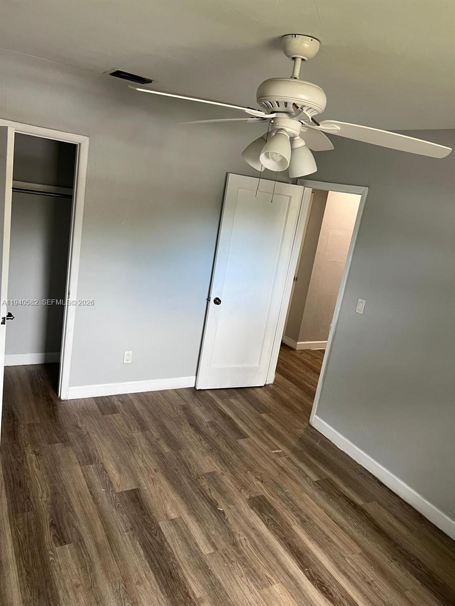 This bedroom features gray walls, wood-look flooring, a ceiling fan, and two open doorways — 130 NE 171st Ter, Miami FL 33162, MIAMI, FL