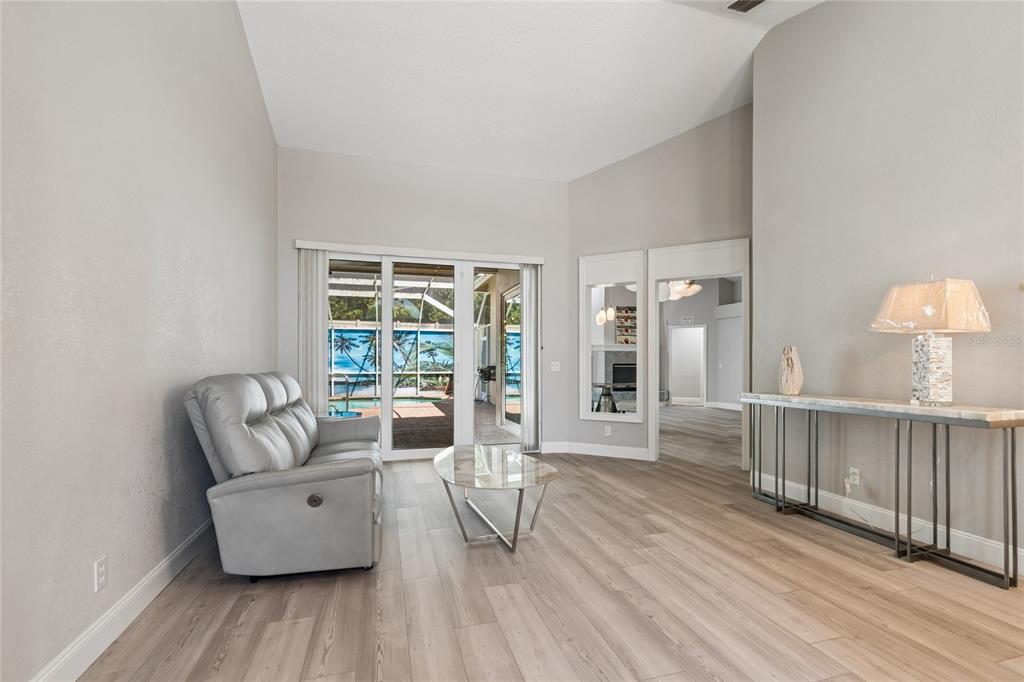 A living room features light wood-look flooring, a grey recliner, and sliding glass doors to a pool — 4227 AUSTON WAY, PALM HARBOR, FL