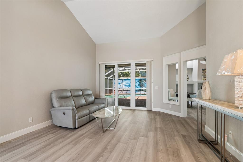 A living room with light wood flooring, a gray sofa, and sliding glass doors to a pool — 4227 AUSTON WAY, PALM HARBOR, FL