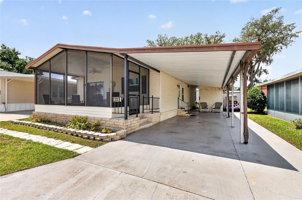 A single-story mobile home features a screened-in porch, a concrete driveway, and a metal carport — 572 TAMMI DRIVE, LEESBURG, FL