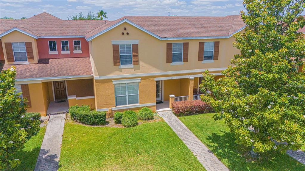 An exterior view of two adjacent townhomes with yellow stucco walls and brown shingled roofs — 10934 SAVANNAH LANDING CIRCLE, ORLANDO, FL
