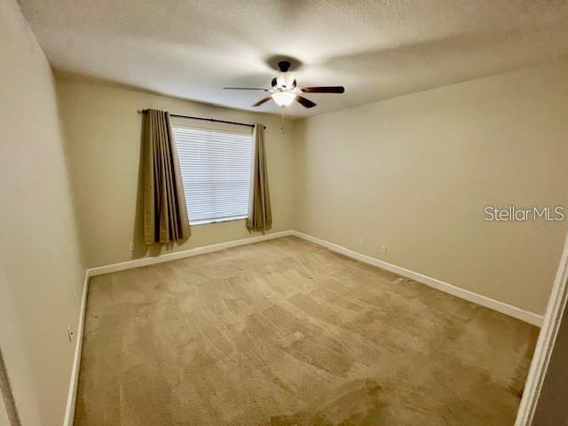 An empty bedroom features beige walls, tan carpeting, a ceiling fan, and a window with curtains — 10934 SAVANNAH LANDING CIRCLE, ORLANDO, FL