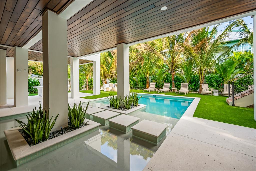 A covered patio overlooks a swimming pool with stepping stones and a surrounding artificial turf lawn — 107 MAPLE AVENUE, ANNA MARIA, FL
