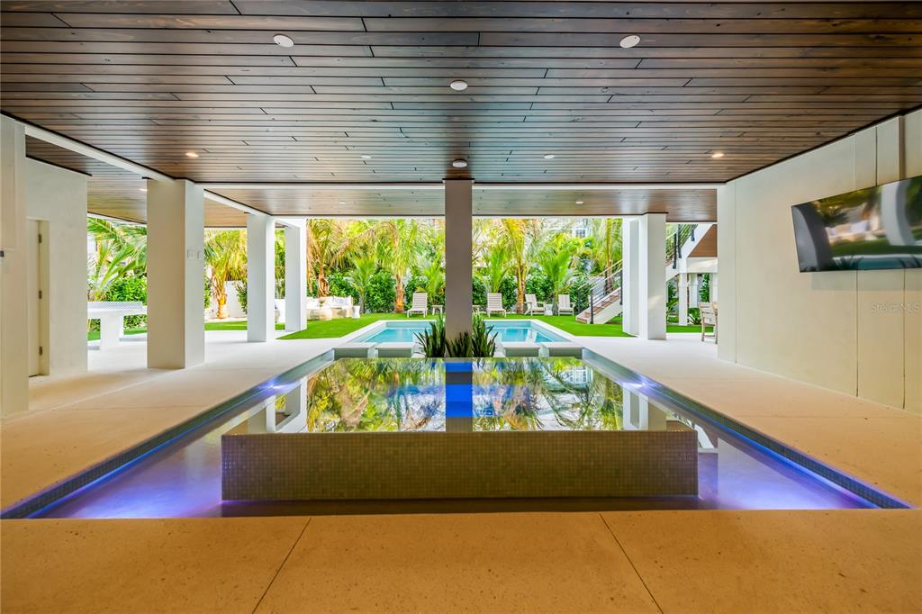 A covered outdoor patio features a central reflecting pool, recessed lighting, and a view of a pool — 107 MAPLE AVENUE, ANNA MARIA, FL