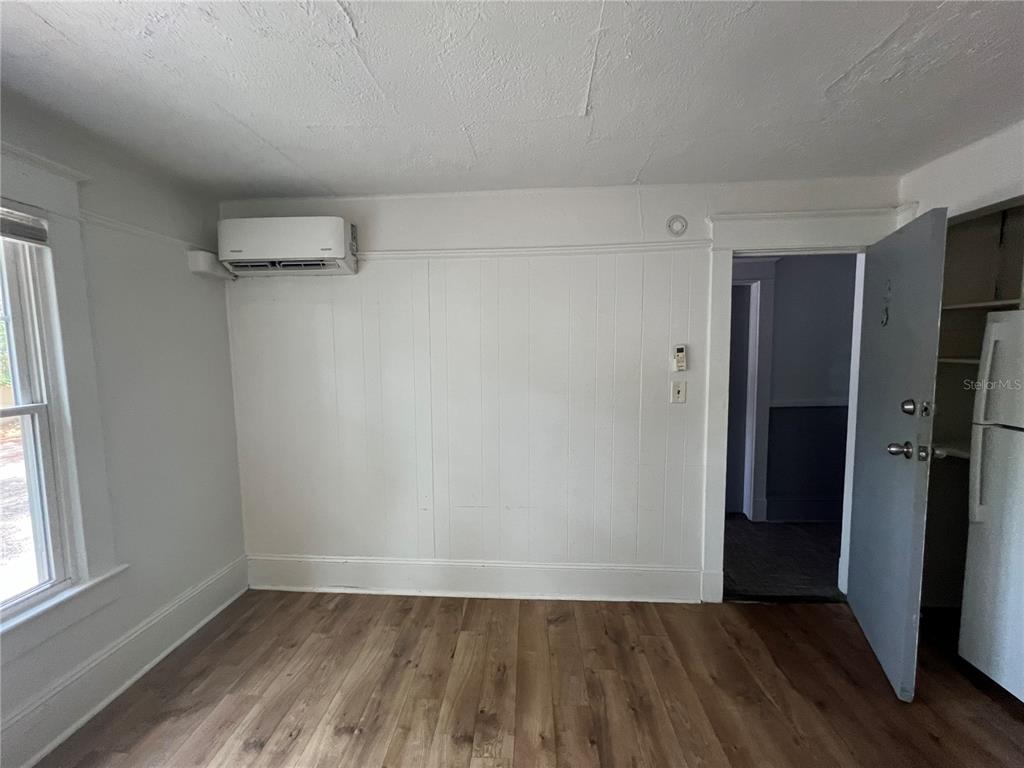 An empty room features wood-look flooring, white walls, a window with blinds, and a wall-mounted AC — 510 E JACKSON ST UNIT 3, ORLANDO, FL