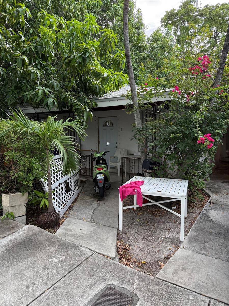 A small house exterior features a green scooter, a white table, and lush tropical landscaping — 414 Virginia Street, Key West FL 33040, KEY WEST, FL