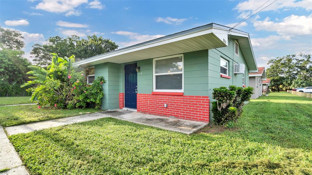 A single-story house with green siding, a red brick accent wall, and a blue door — 5526 59TH WAY N UNIT 1, ST PETERSBURG, FL