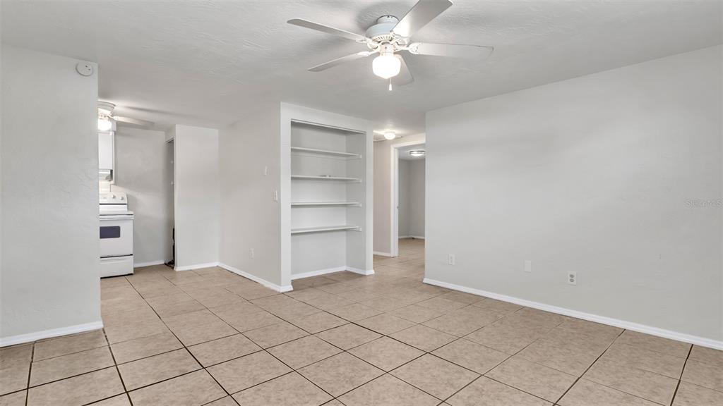 A living room with light-colored walls, tile flooring, a ceiling fan, and built-in shelving — 5526 59TH WAY N UNIT 1, ST PETERSBURG, FL