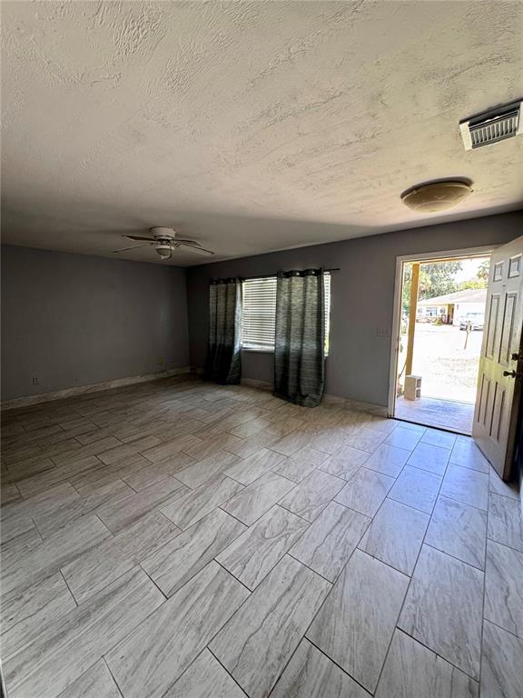 An empty room features gray walls, light wood-look tile flooring, a ceiling fan, and an exterior door — 920 BOULDER DRIVE, SOUTH DAYTONA, FL