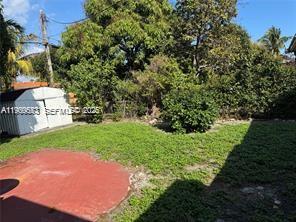 A backyard features a small white shed, a red patio area, and mature green trees — 1077 NE 157th Ter, North Miami Beach FL 33162, NORTH MIAMI BEACH, FL