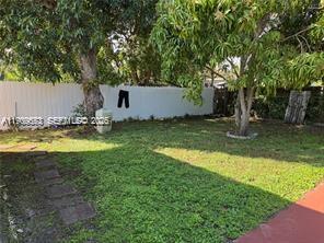 A grassy backyard features a white fence, mature trees, and a stone path — 1077 NE 157th Ter, North Miami Beach FL 33162, NORTH MIAMI BEACH, FL