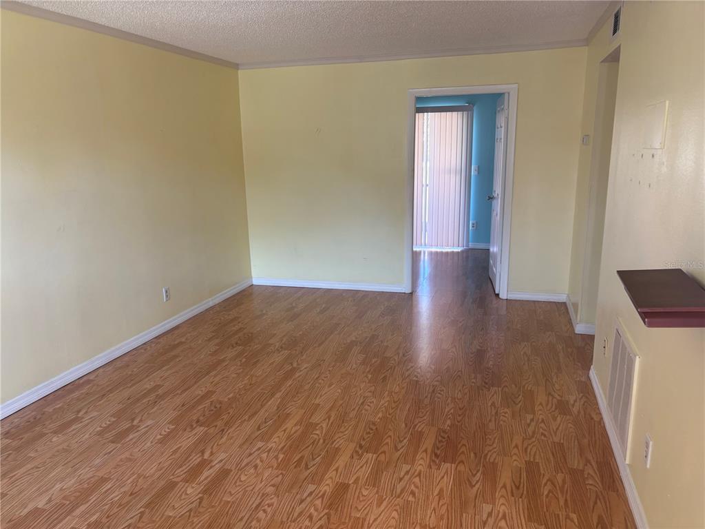An empty room with light yellow walls and wood-look flooring leads to a doorway — 24862 US HIGHWAY 19 N UNIT 205, CLEARWATER, FL