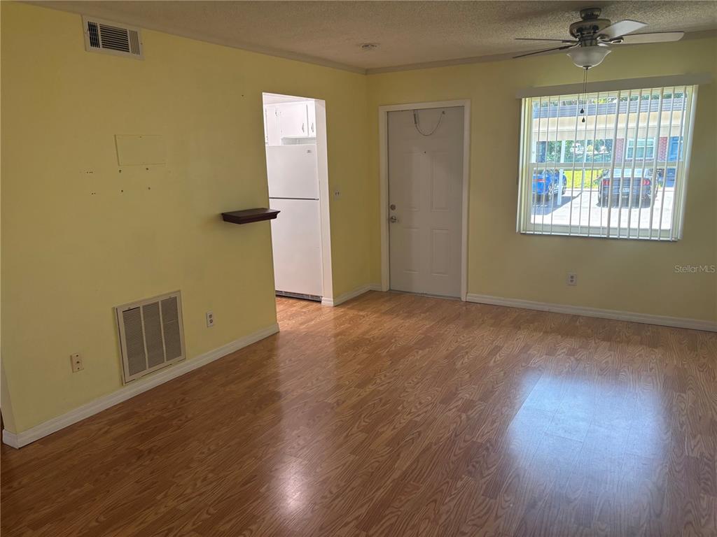 A living room with light yellow walls, wood-look flooring, a ceiling fan, and a kitchen view — 24862 US HIGHWAY 19 N UNIT 205, CLEARWATER, FL
