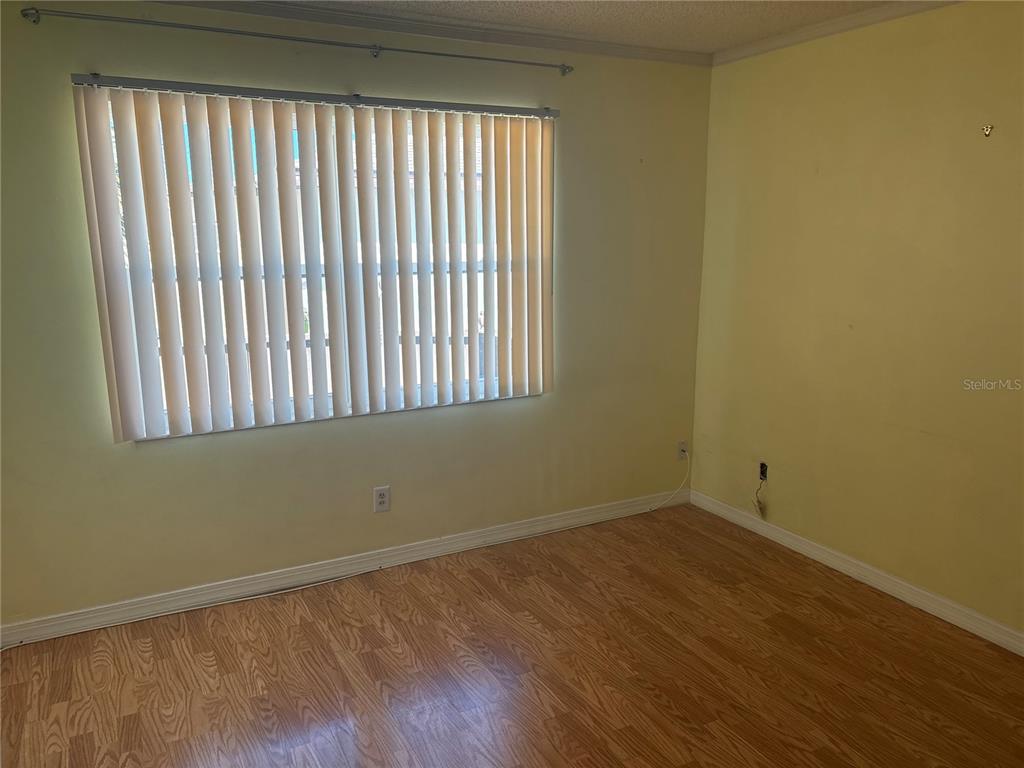 An empty room with light yellow walls, wood-look flooring, and vertical window blinds — 24862 US HIGHWAY 19 N UNIT 205, CLEARWATER, FL