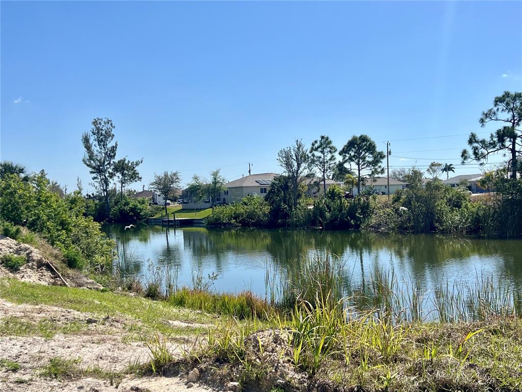 A view of a calm pond with surrounding trees and houses in the background — 504 NW 20TH STREET, CAPE CORAL, FL