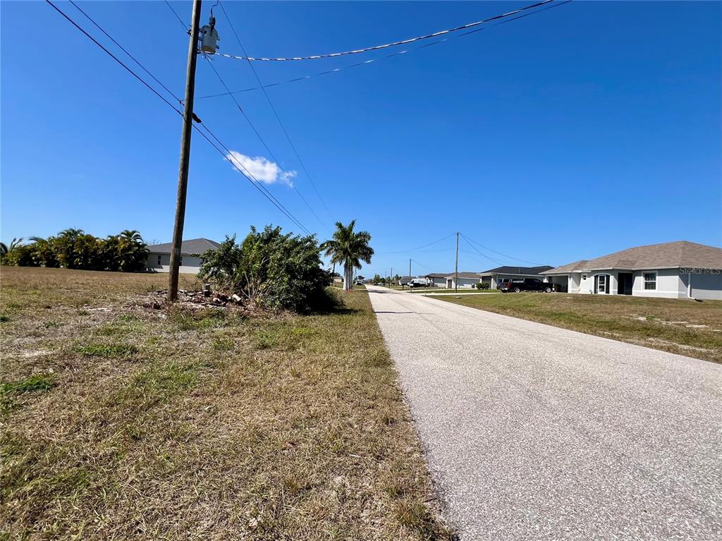 A paved street runs between a grassy lot with a utility pole and suburban houses — 504 NW 20TH STREET, CAPE CORAL, FL