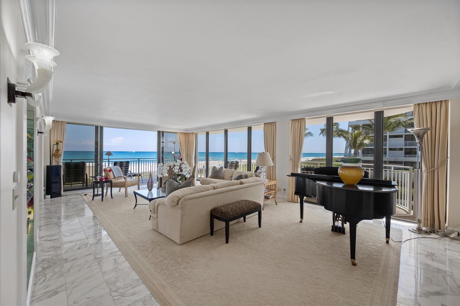 A living room with a grand piano, beige sofa, and floor-to-ceiling windows overlooking the ocean — 2580 S Ocean Boulevard, Palm Beach FL 33480, PALM BEACH, FL