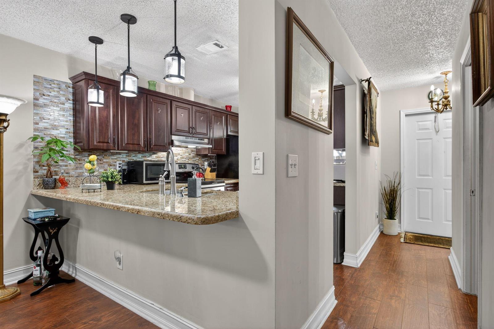 A kitchen with dark wood cabinets, granite countertops, and a breakfast bar overlooks a hallway — 2122 NE 44th Street, Lighthouse Point FL 33064, LIGHTHOUSE POINT, FL