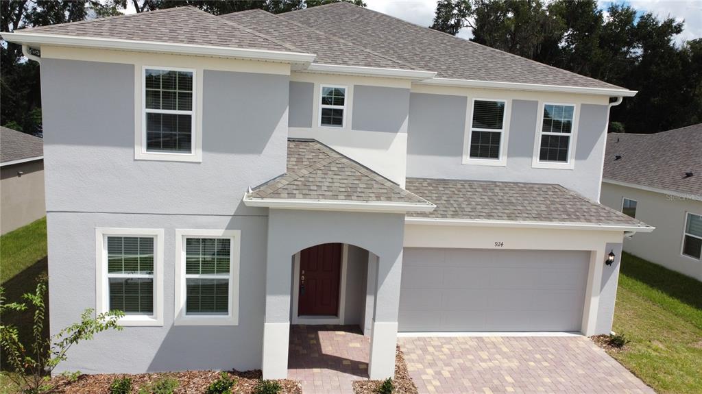 A two-story gray house with a red front door, a garage, and a paved driveway — 924 AVENAL LANE, DAVENPORT, FL