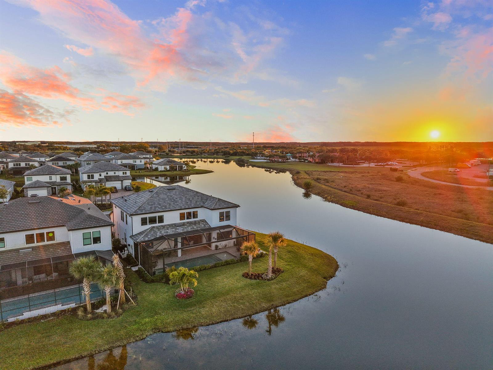 An aerial view shows houses with screened pools along a lake at sunset — 4107 Traditions Drive, Ave Maria FL 34142, AVE MARIA, FL