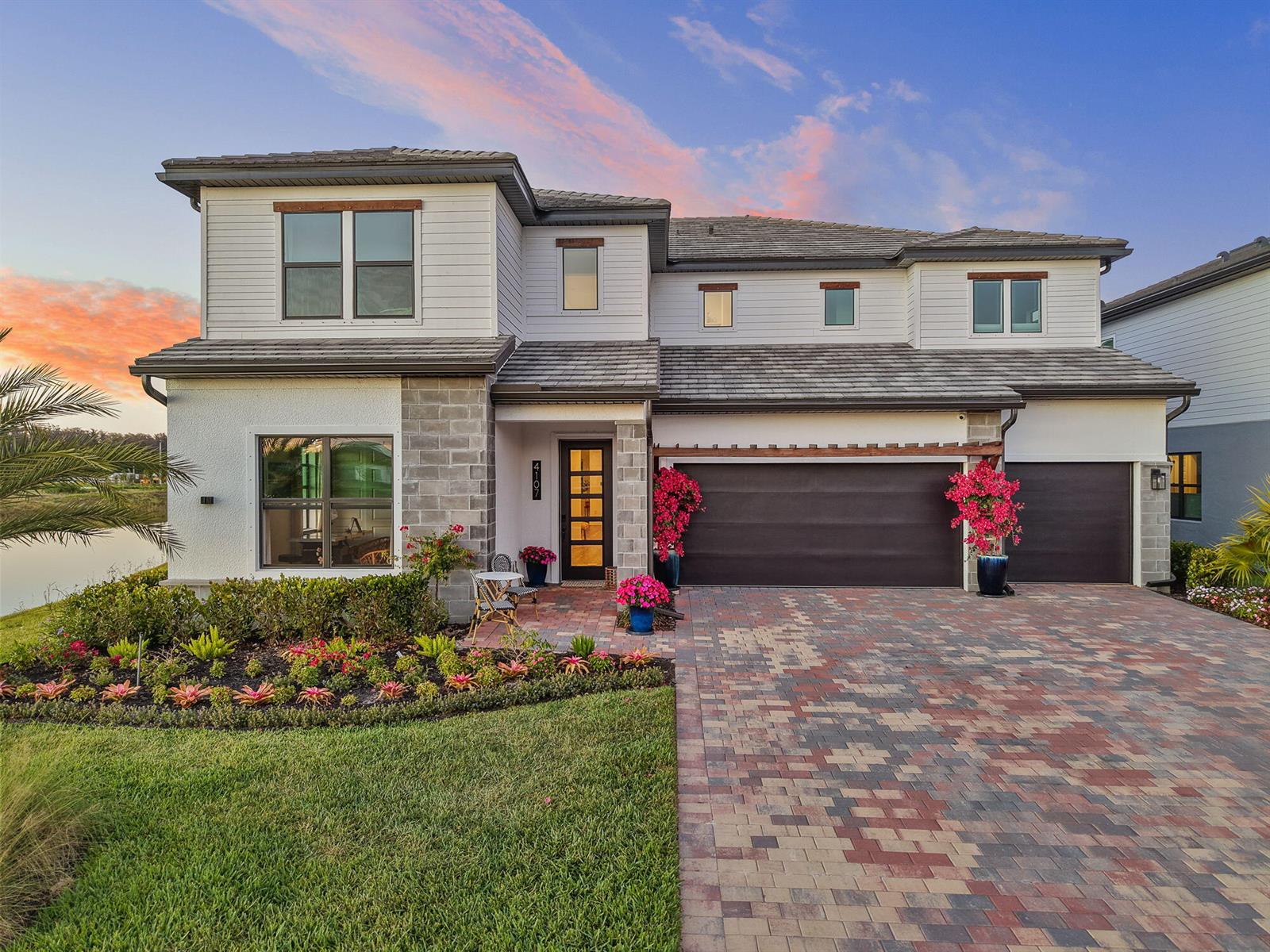 A two-story house with a stone facade, multi-car garage, and a paved driveway at sunset — 4107 Traditions Drive, Ave Maria FL 34142, AVE MARIA, FL