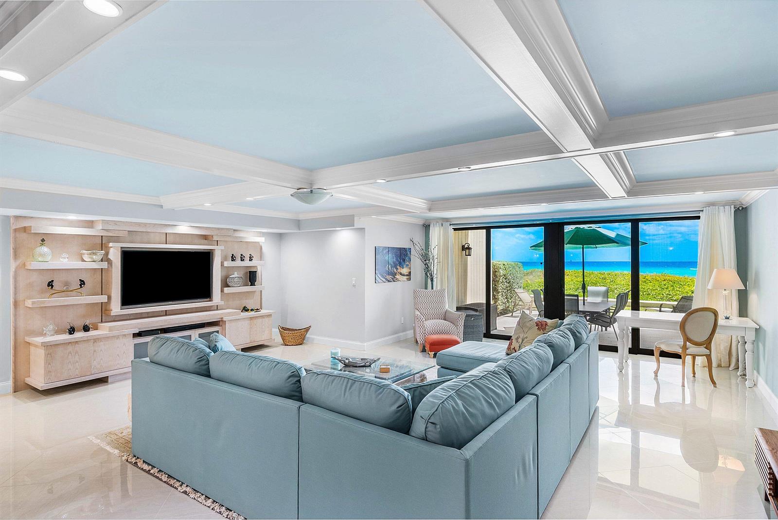 A living room features a blue sectional sofa, coffered ceiling, and sliding doors overlooking the ocean — 2155 S Ocean Boulevard # 7, Delray Beach FL 33483, DELRAY BEACH, FL