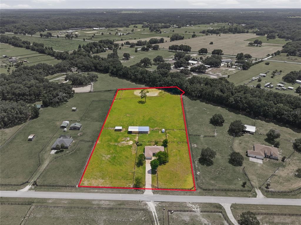 An aerial view shows a house and outbuildings on a fenced, rectangular rural property — 19630 SE 15TH PLACE, MORRISTON, FL
