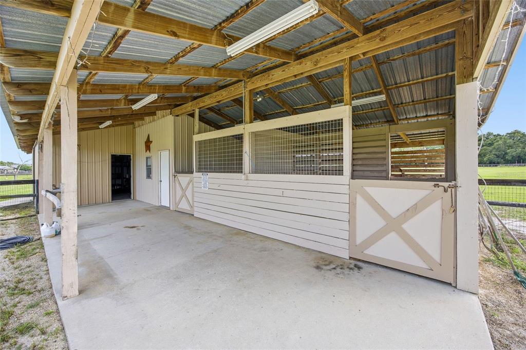 A covered outdoor horse stable with concrete flooring, wooden stalls, and metal roofing — 19630 SE 15TH PLACE, MORRISTON, FL