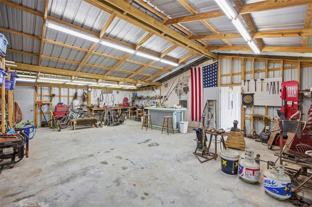 A spacious workshop with a concrete floor, exposed wooden rafters, and various tools and equipment — 19630 SE 15TH PLACE, MORRISTON, FL