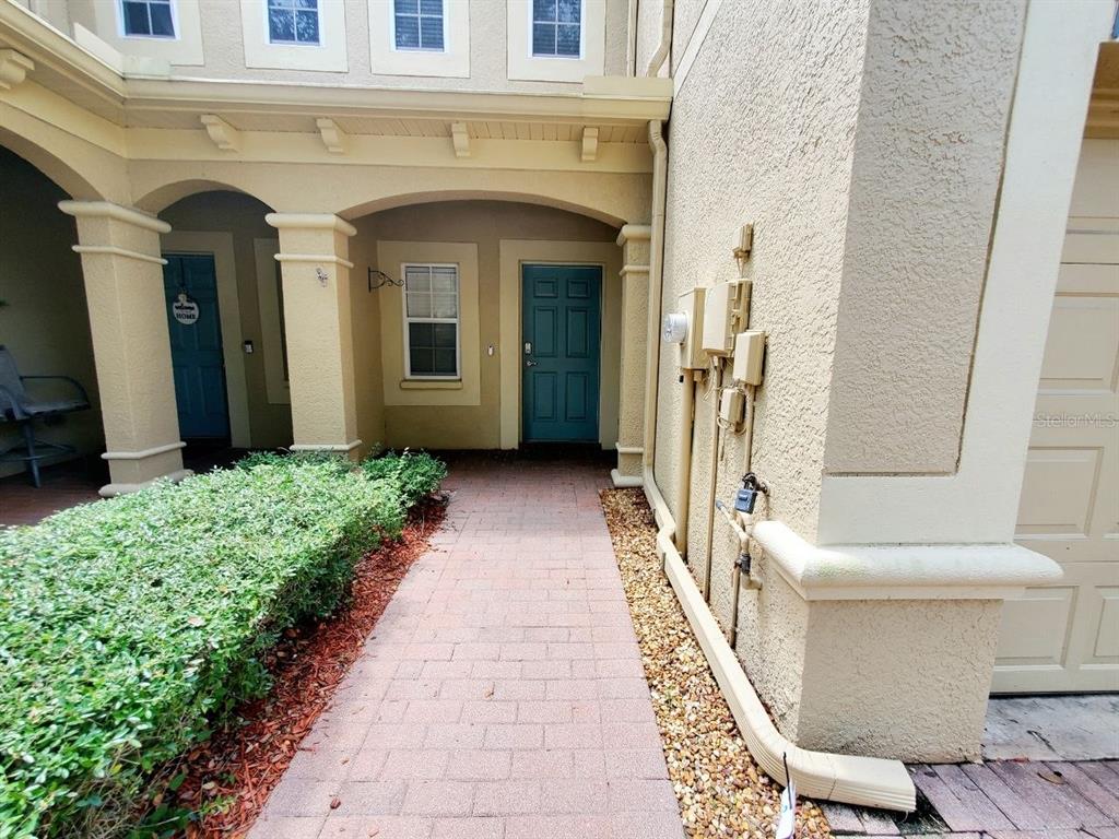 A paved walkway leads to a covered entryway with two blue doors and stucco walls — 17532 HUGH LANE, LAND O LAKES, FL
