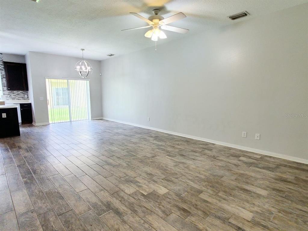 An open-concept living and dining area features light gray walls and wood-look tile flooring — 17532 HUGH LANE, LAND O LAKES, FL