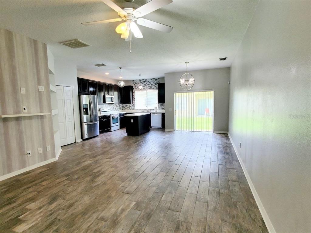 An open-concept kitchen and living area featuring dark cabinetry, a center island, and wood-look flooring — 17532 HUGH LANE, LAND O LAKES, FL