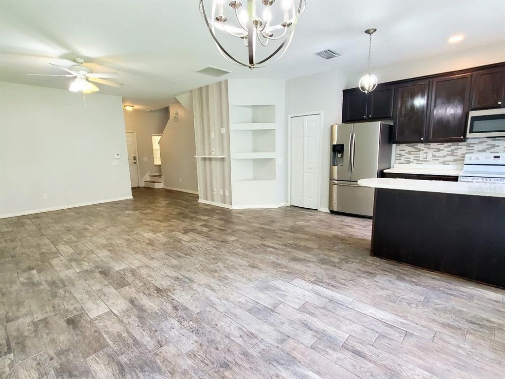 An open-concept kitchen and living area feature wood-look tile flooring and dark wood cabinetry — 17532 HUGH LANE, LAND O LAKES, FL