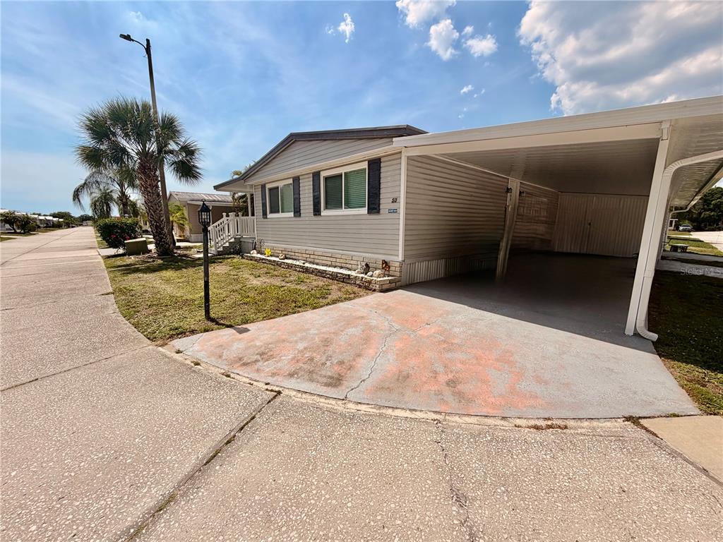 A single-story manufactured home features light gray siding, a carport, and a concrete driveway — 1710 7TH STREET SW UNIT 50, RUSKIN, FL