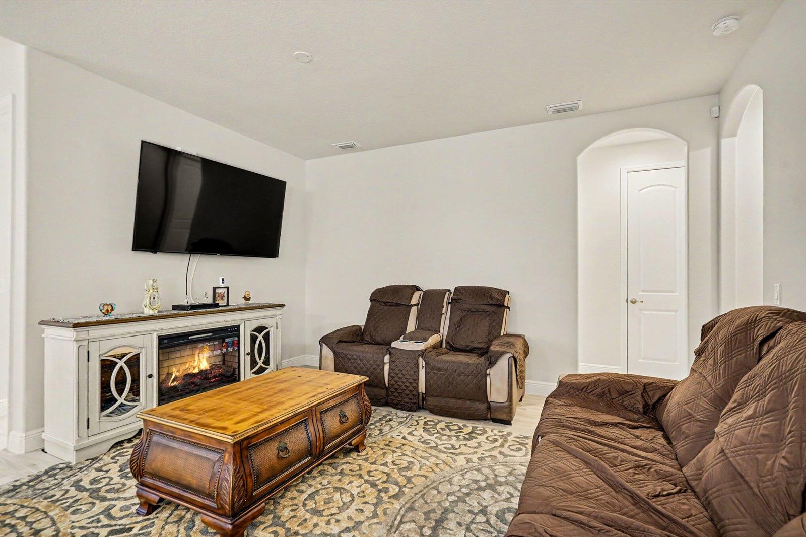 A living room features a wall-mounted television, an electric fireplace console, and brown seating — 2964 Blazing Star Drive, Melbourne FL 32940, MELBOURNE, FL