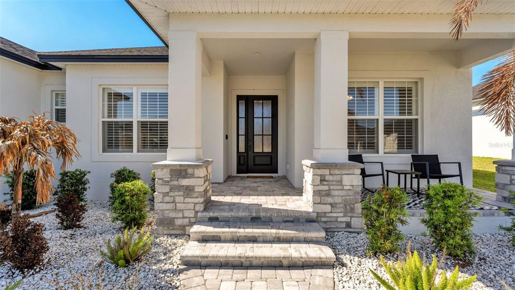 The front entrance of a house features a stone-accented porch, a dark door, and landscaping — 7013 BENTRIDGE DRIVE, LAKELAND, FL