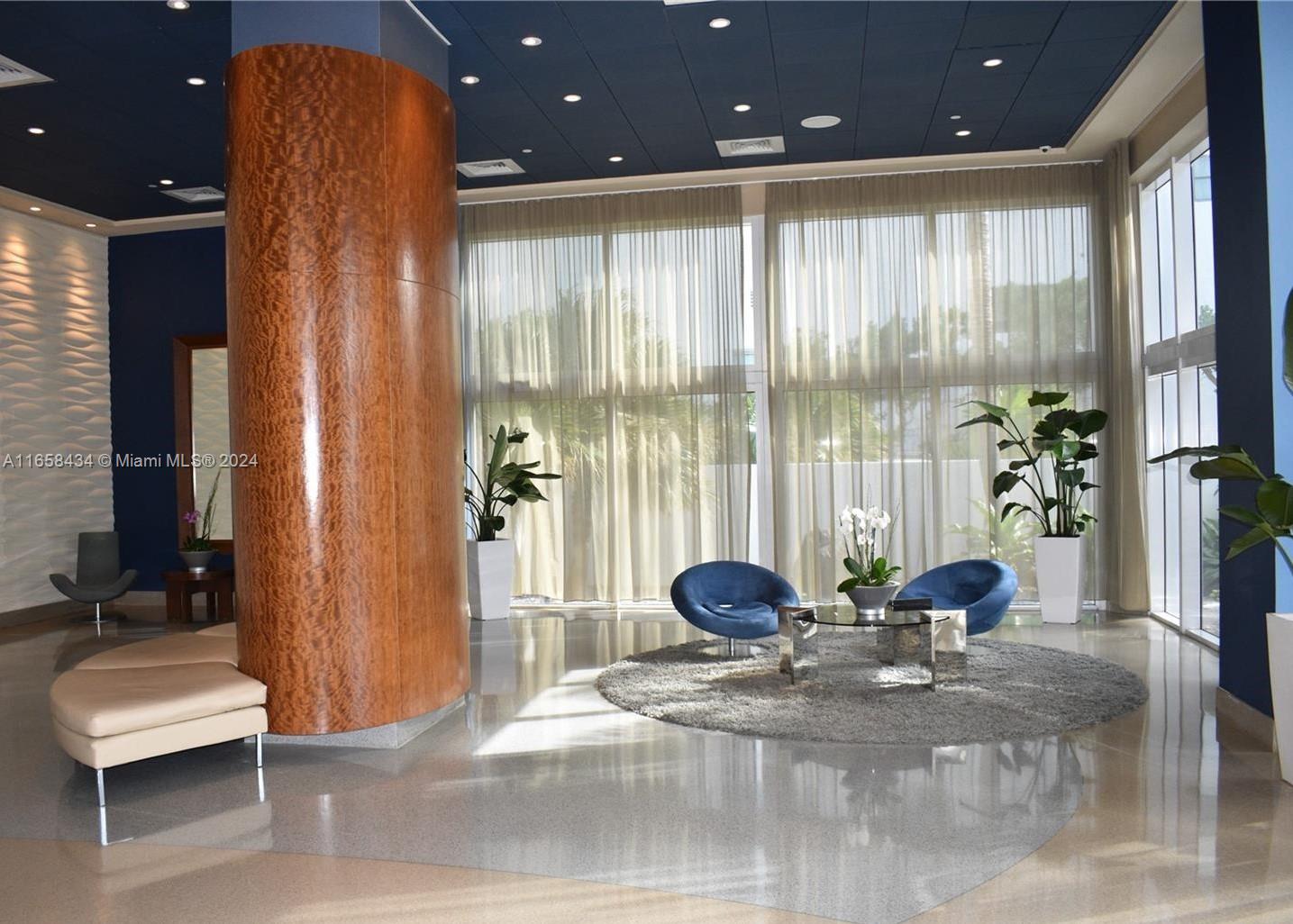 A modern lobby features a large wooden pillar, blue armchairs, and floor-to-ceiling sheer curtains — 6365 Collins Ave # 4209, Miami Beach FL 33141, MIAMI BEACH, FL